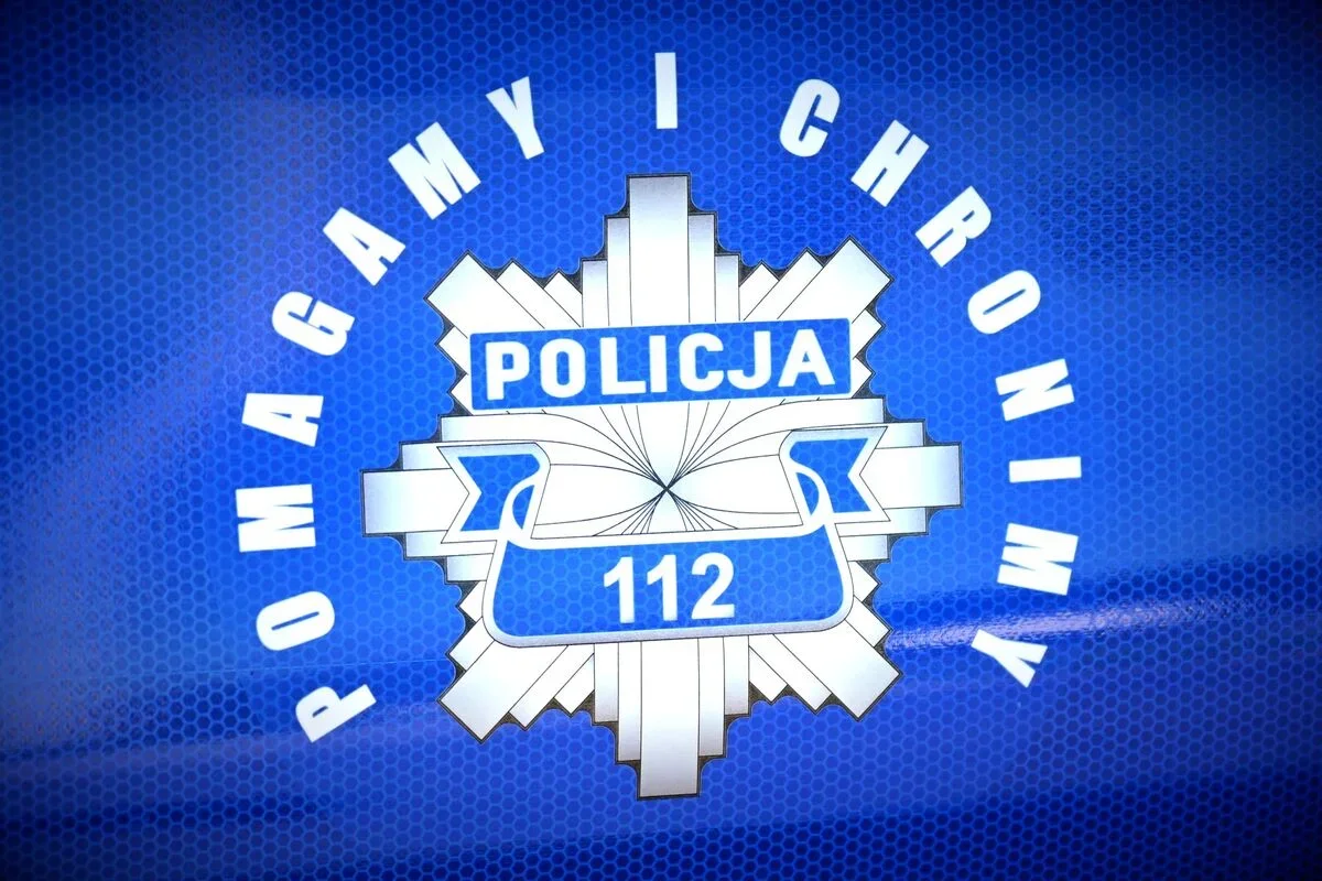 Zbliżenie na niebieski znak policyjny z napisami „POMAGAMY I CHRONIMY”, „POLICJA” i numerem alarmowym „112” na tle siateczkowej faktury.