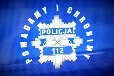 Zbliżenie na niebieski znak policyjny z napisami „POMAGAMY I CHRONIMY”, „POLICJA” i numerem alarmowym „112” na tle siateczkowej faktury.